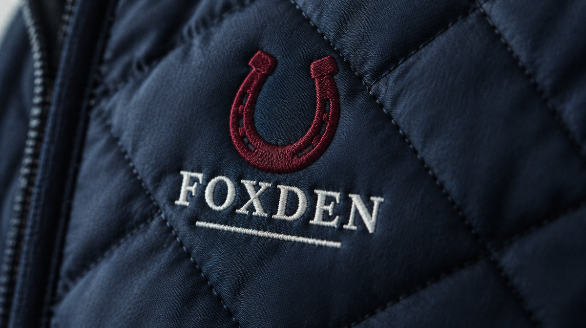 Close-up of embroidered crest and wordmark on a navy quilted gilet